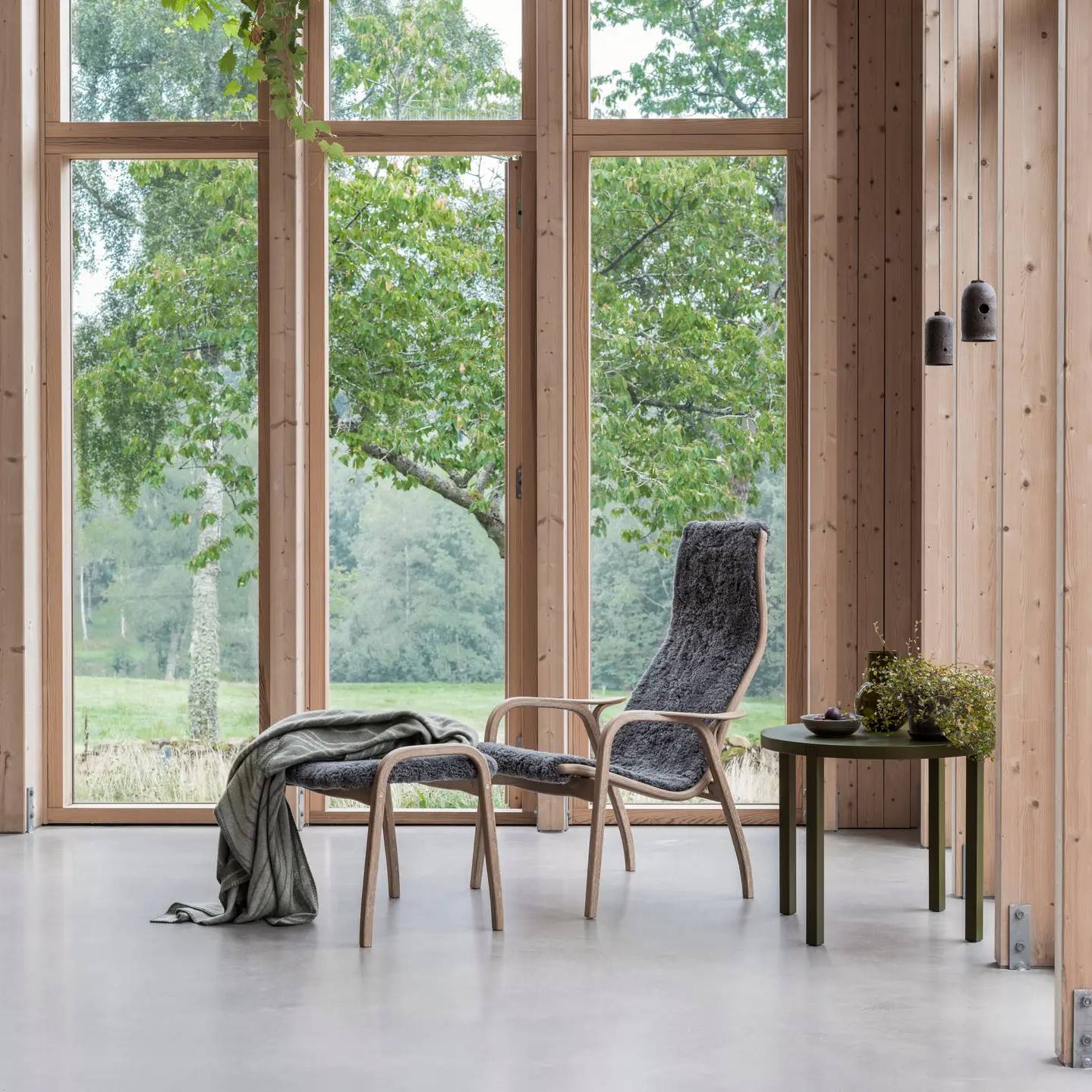 Lamino-Fußhocker | Swedese | Lundia Living mit geschwungenem Holzrahmen und anthrazitgrauem, weichem Bezug in einem hellen Raum mit Aussicht