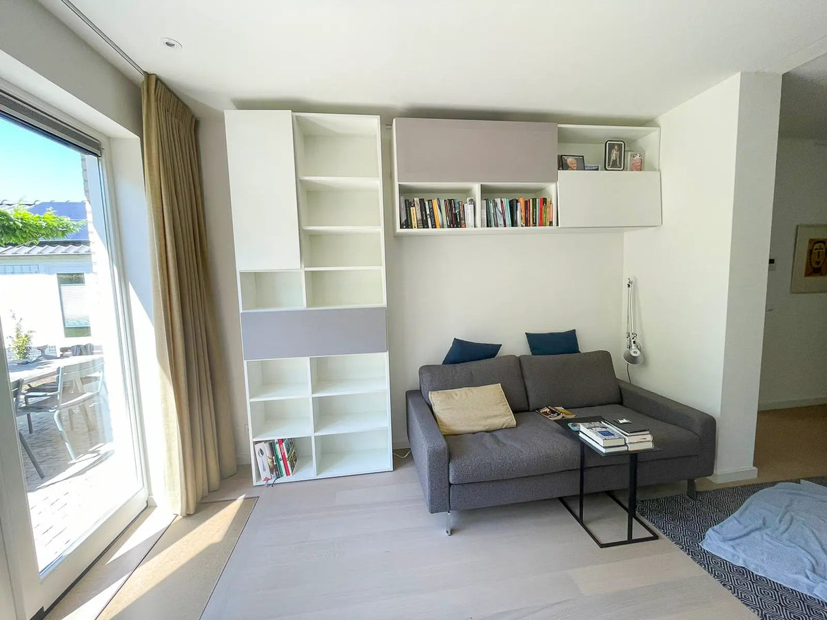 Witte boekenkast op maat van Lundia met hangend wandelement boven de bank
