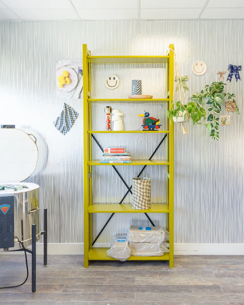 Felgele open kast met diverse decoratieve objecten en hangende groene plant voor gestreepte witte muur