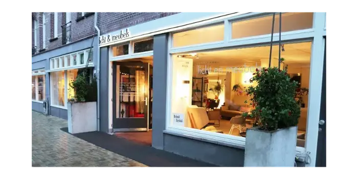 Vooraanzicht van moderne winkel met grote ramen en sfeervolle verlichting in een straat met natte klinkers.