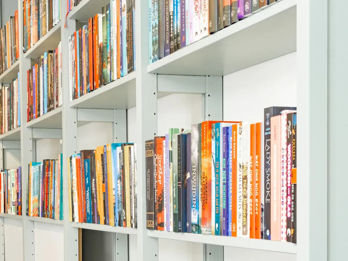 Witte boekenplanken gevuld met diverse kleurrijke boeken in een helder verlichte ruimte zonder mensenzichtbaar