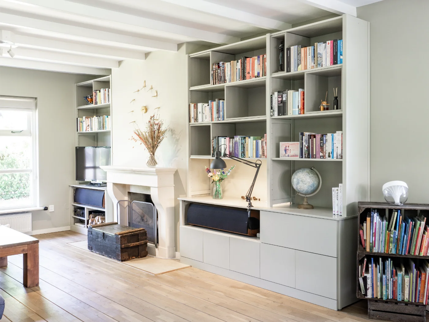 Helles Wohnzimmer mit Holzboden, Einbaubücherregalen, Kamin und Fenster mit Tageslicht
