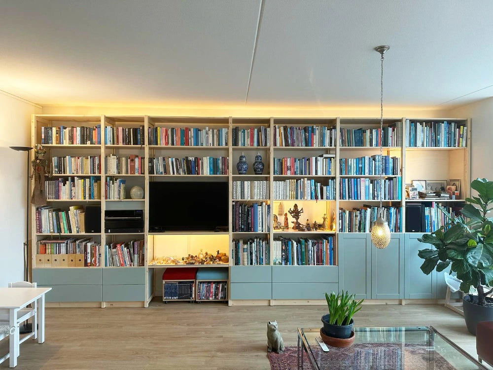 Ruime wandkast gevuld met boeken, sfeerverlichting en decoratieve objecten in een lichte woonkamer met houten vloer.