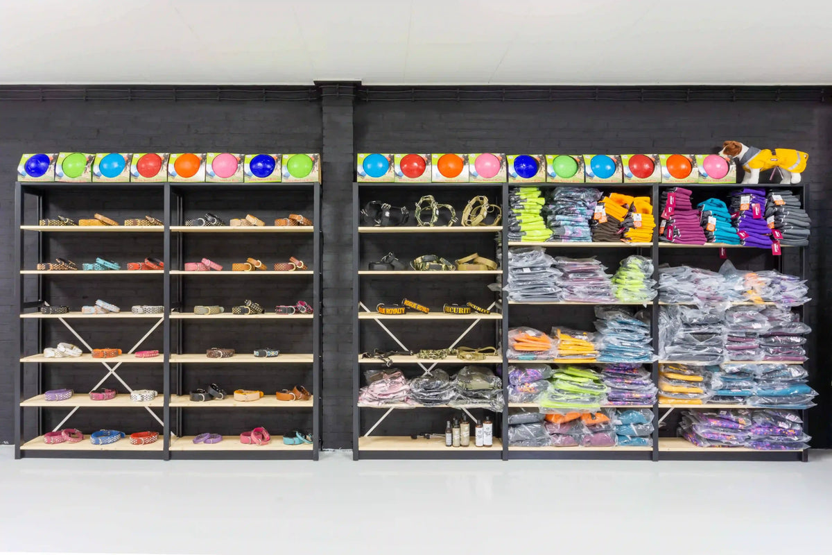 Zwarte metalen rekken tegen donkere muur met kleurrijke ballonnen en diverse stoffen en houten voorwerpen erop verdeeld.